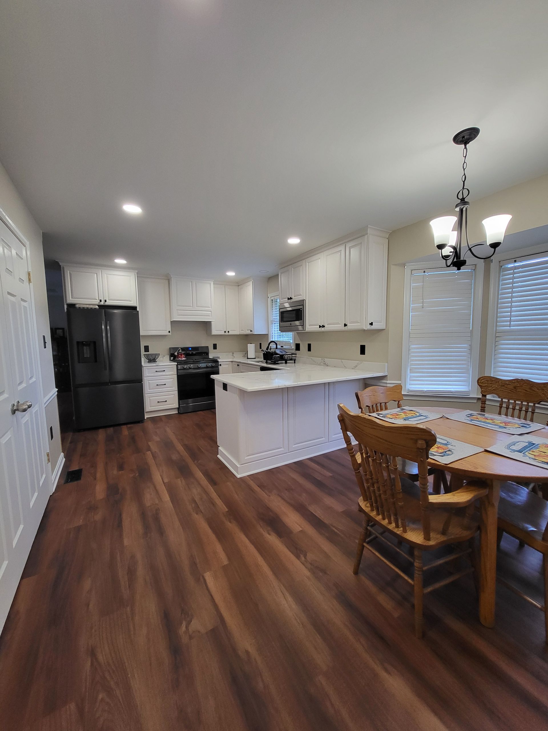 Spacious kitchen with white cabinets, dark refrigerator, and island.  Wood flooring.  Dining table with chairs.