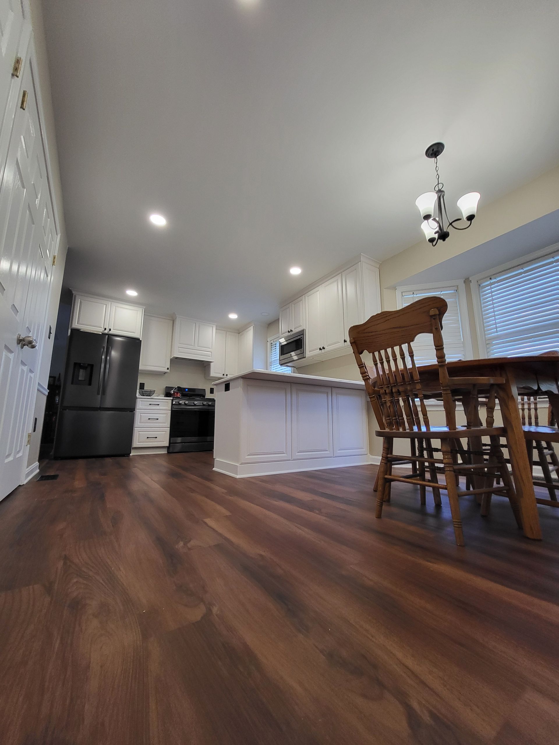 Kitchen with white cabinets, dark wood flooring, black refrigerator, and a wooden dining table.