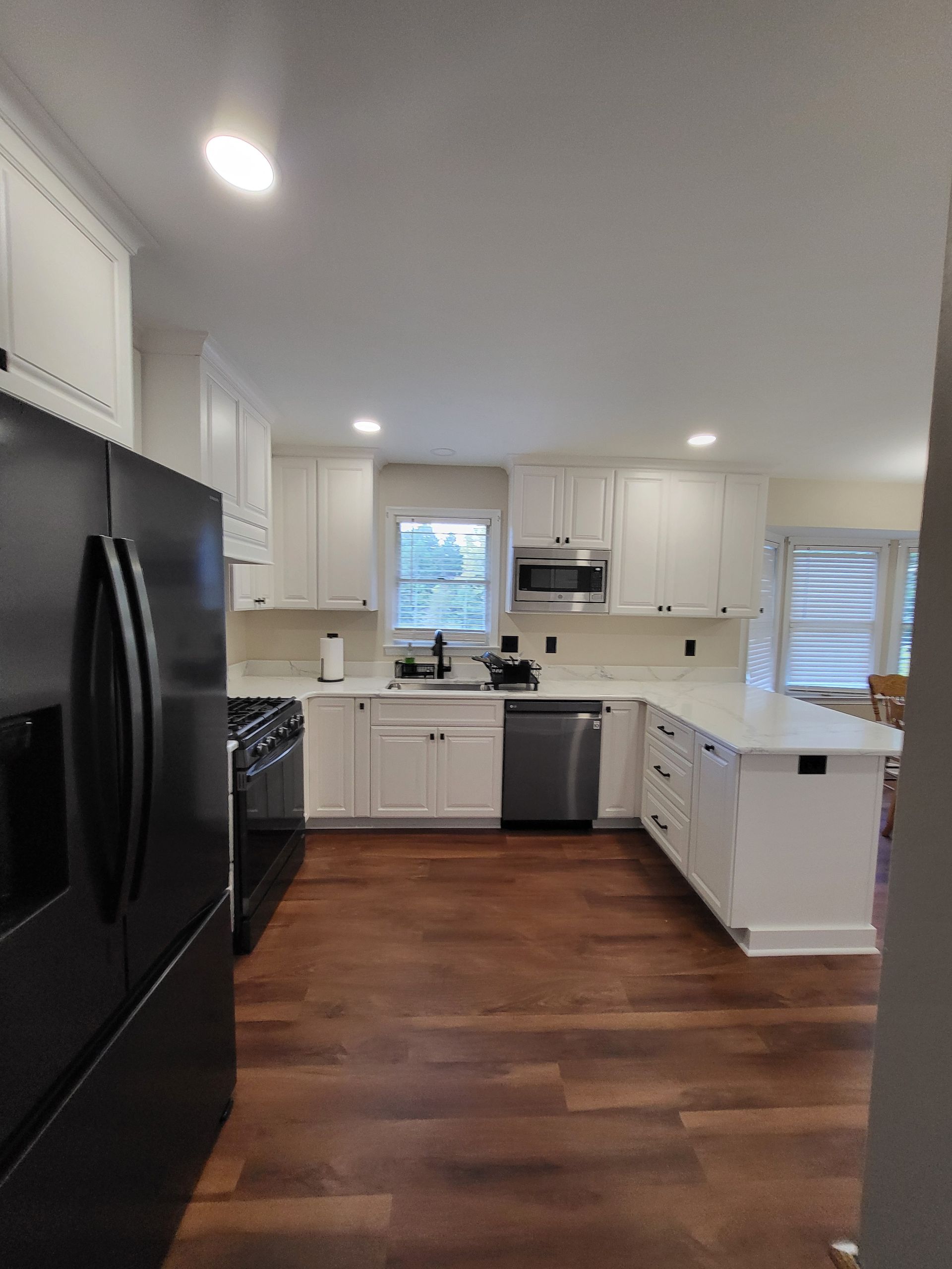 Modern white kitchen with dark wood floors and black appliances.