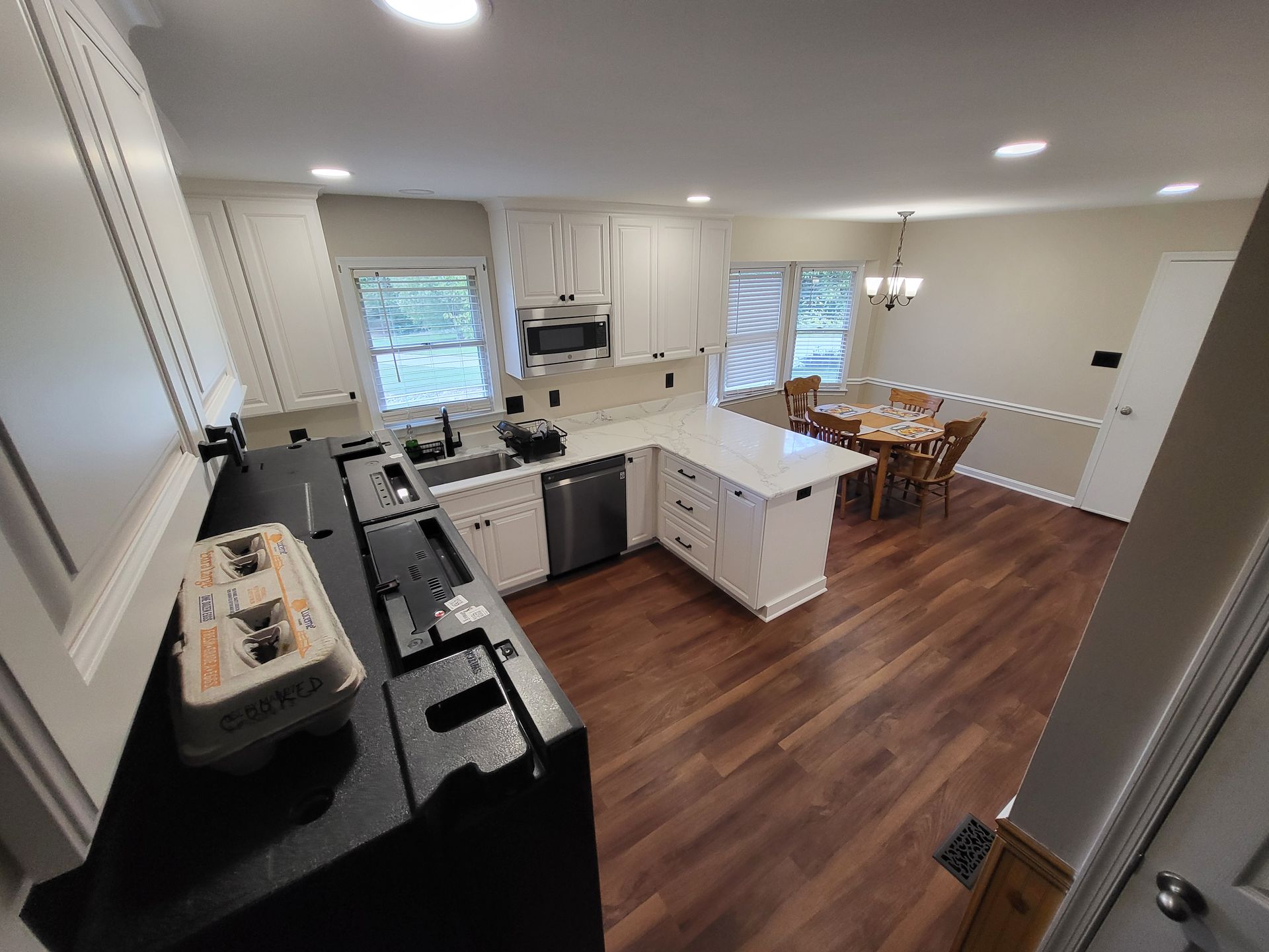 White kitchen with black countertops, stainless steel appliances, and a wooden floor.