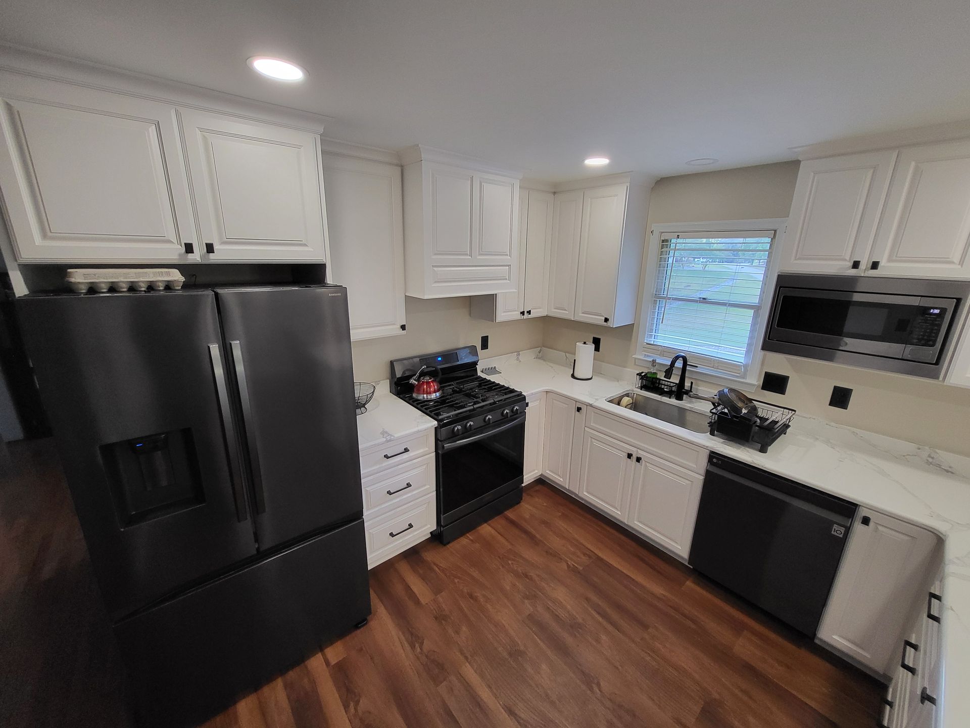 A kitchen with white cabinets, black appliances, and wooden floors.