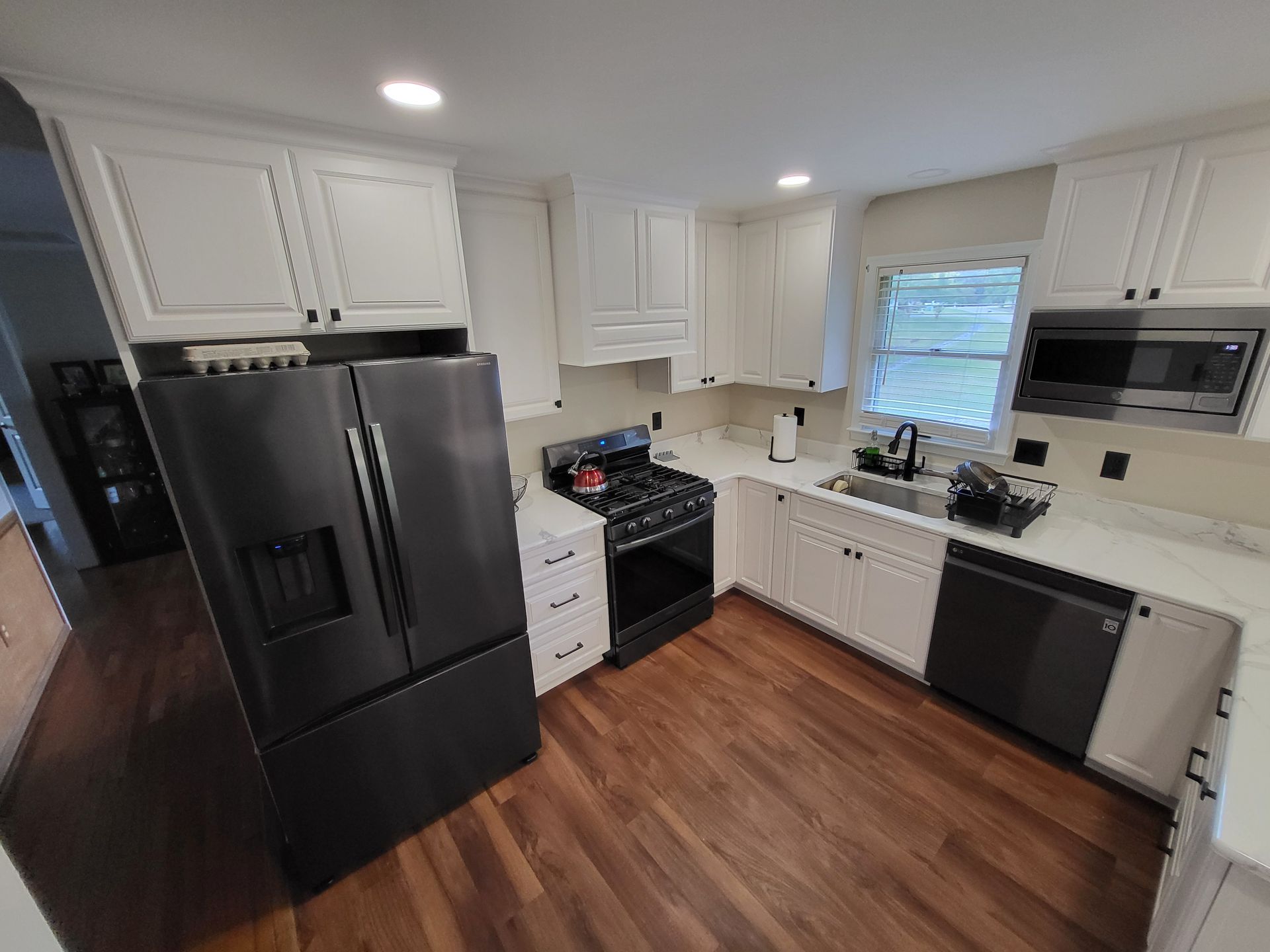 Kitchen with white cabinets, black appliances, and wood-look flooring.