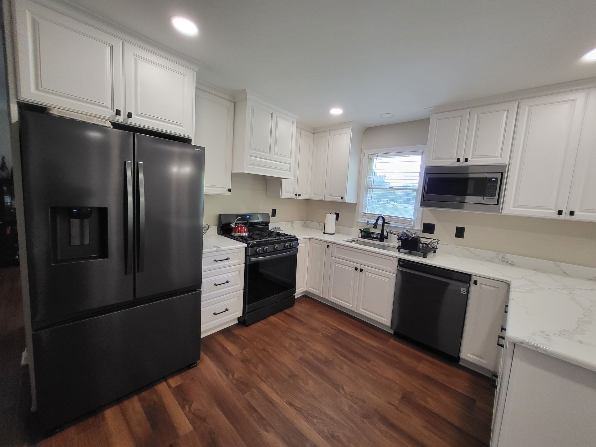 Modern kitchen with white cabinets, dark appliances, and wood floors.