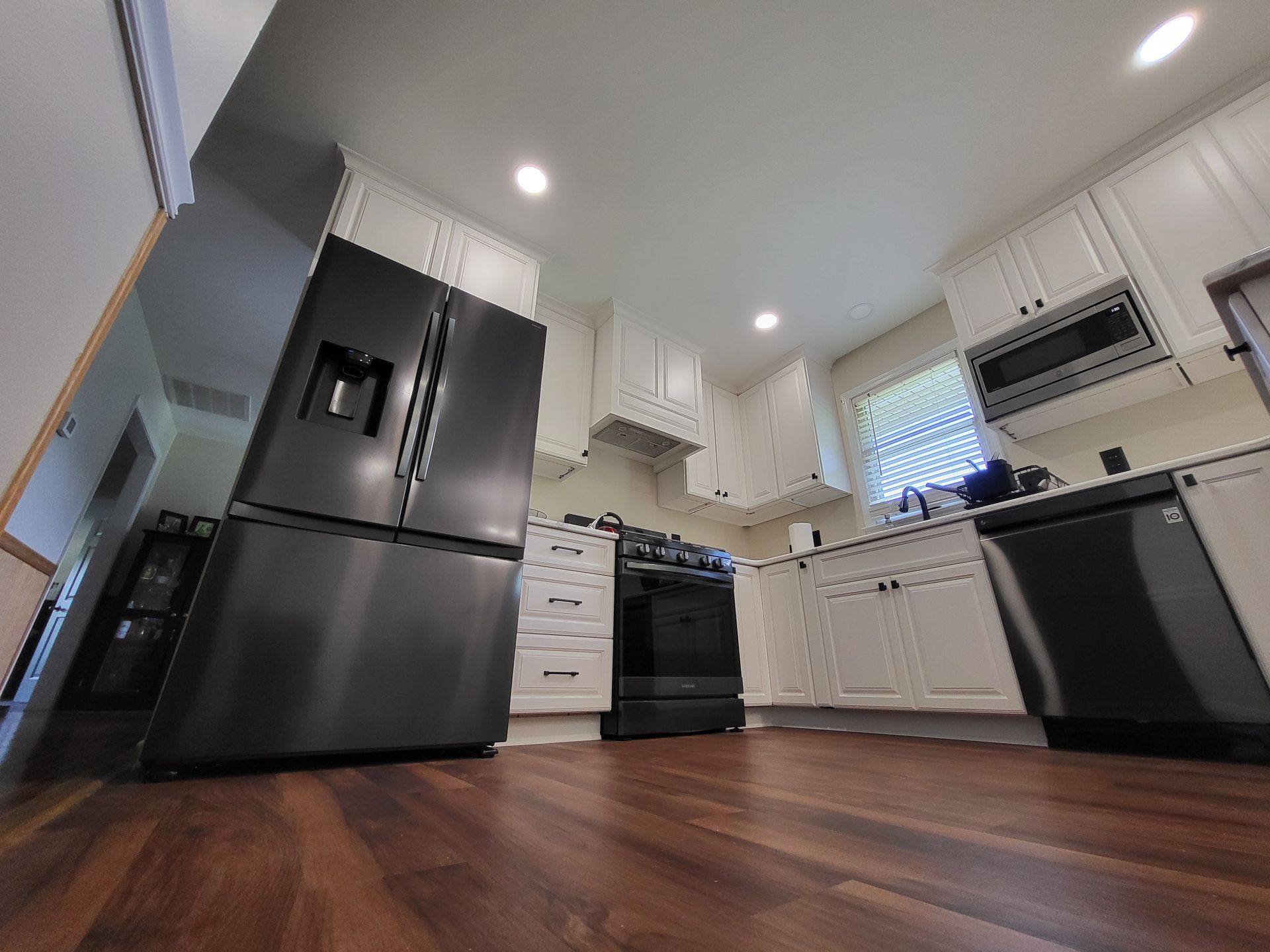 A kitchen with white cabinets, black appliances, and dark wooden floors.