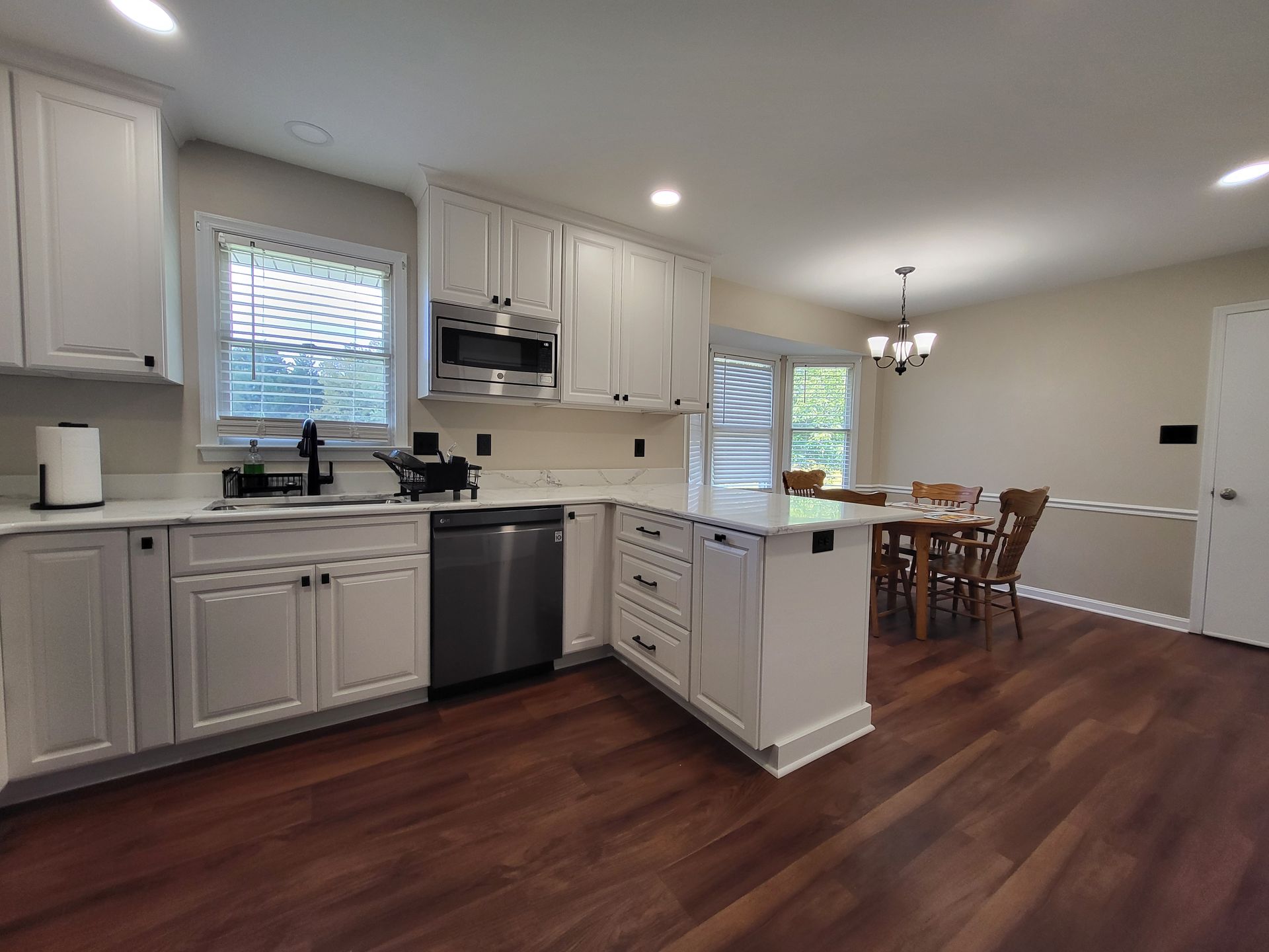 White kitchen with island, stainless steel appliances, and dark wood floors. Dining area in the background.