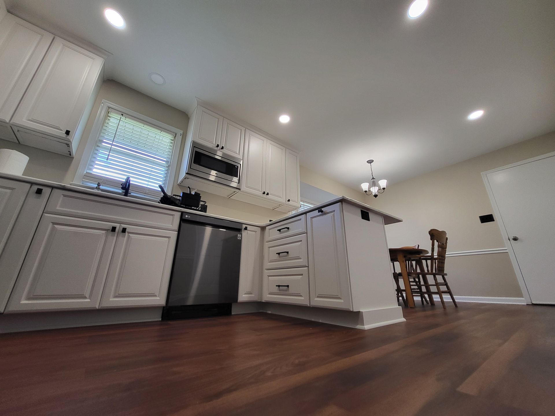 White kitchen with stainless steel appliances, dark wood floors, and island.