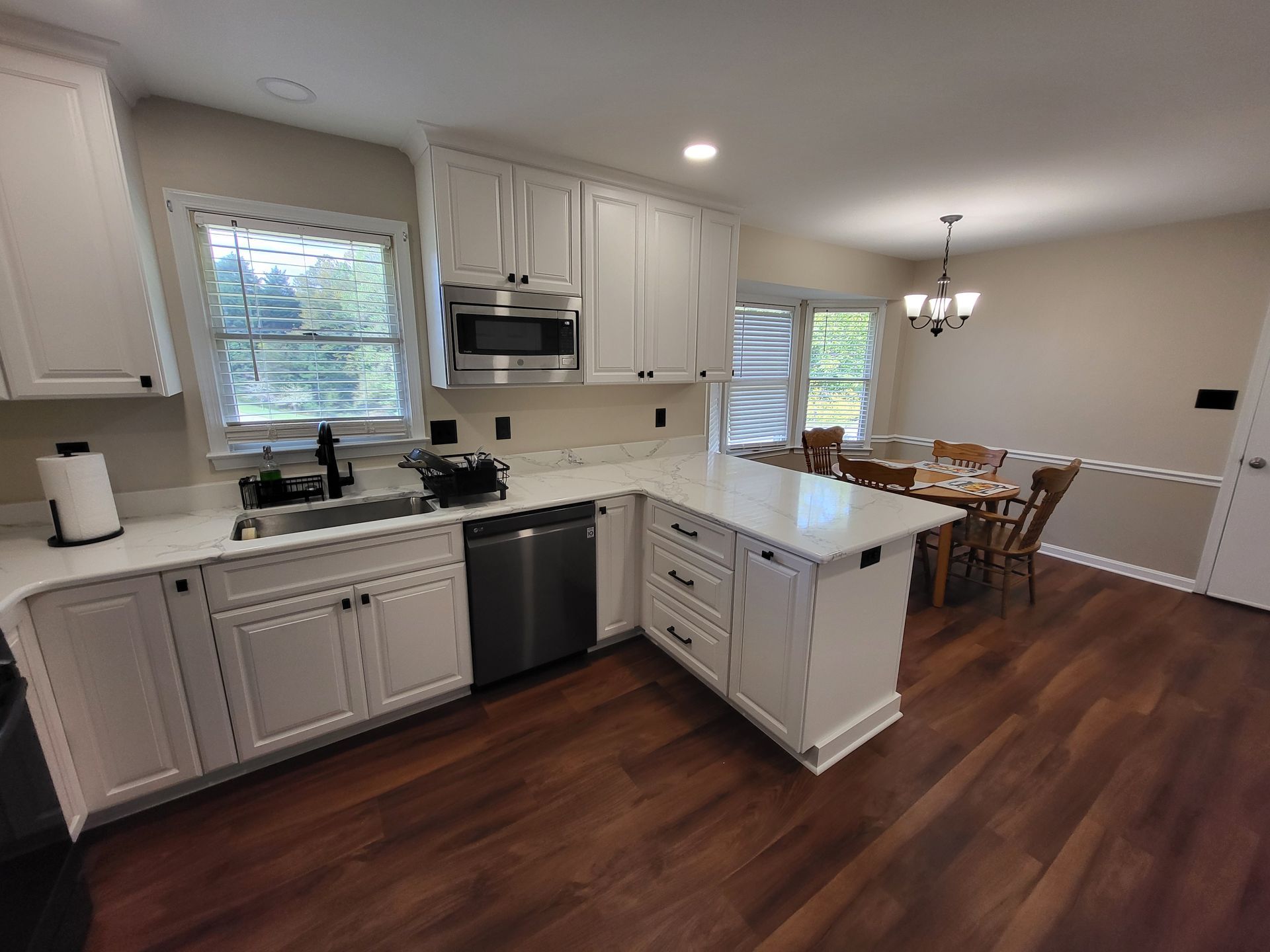 White kitchen with island, stainless steel appliances, and dark wood floors. Dining area in the background.