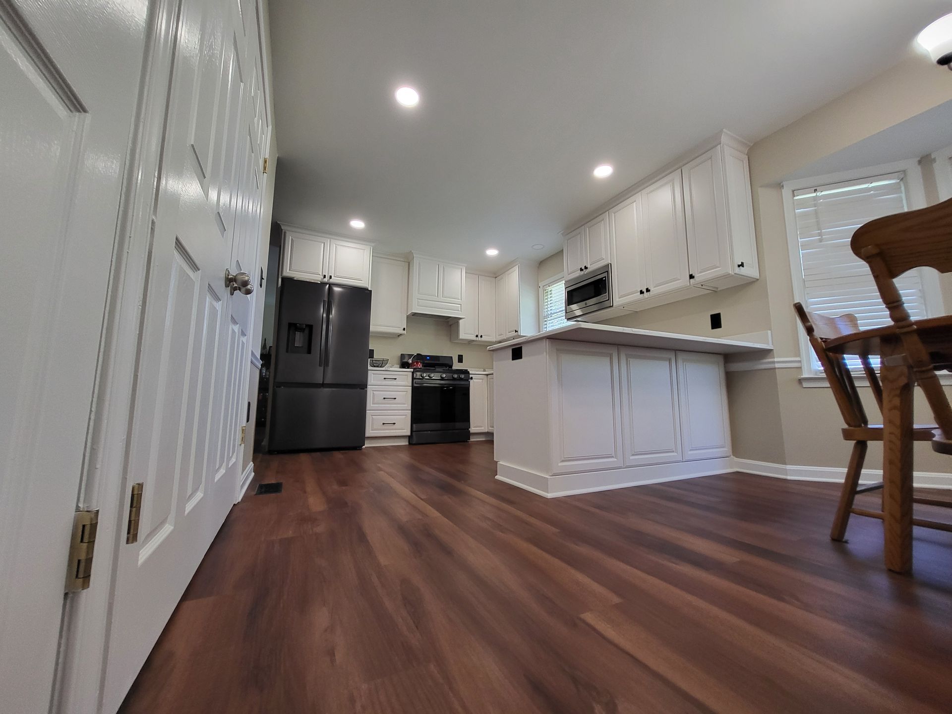 White kitchen with wood flooring, cabinets, and appliances. A table and chairs sit near a window.