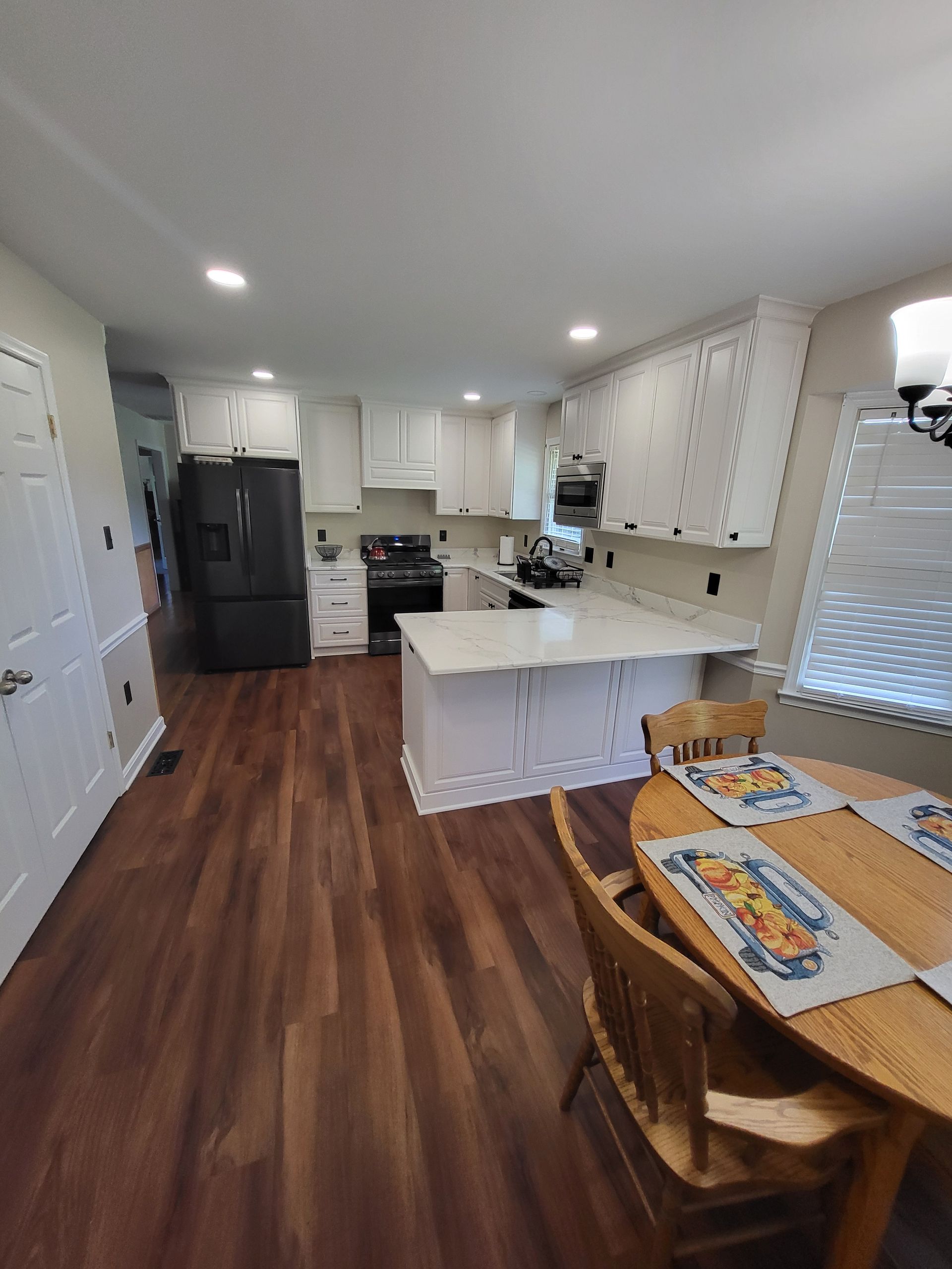 Kitchen with white cabinets, dark refrigerator, island, and wooden floor. Dining table with placemats.