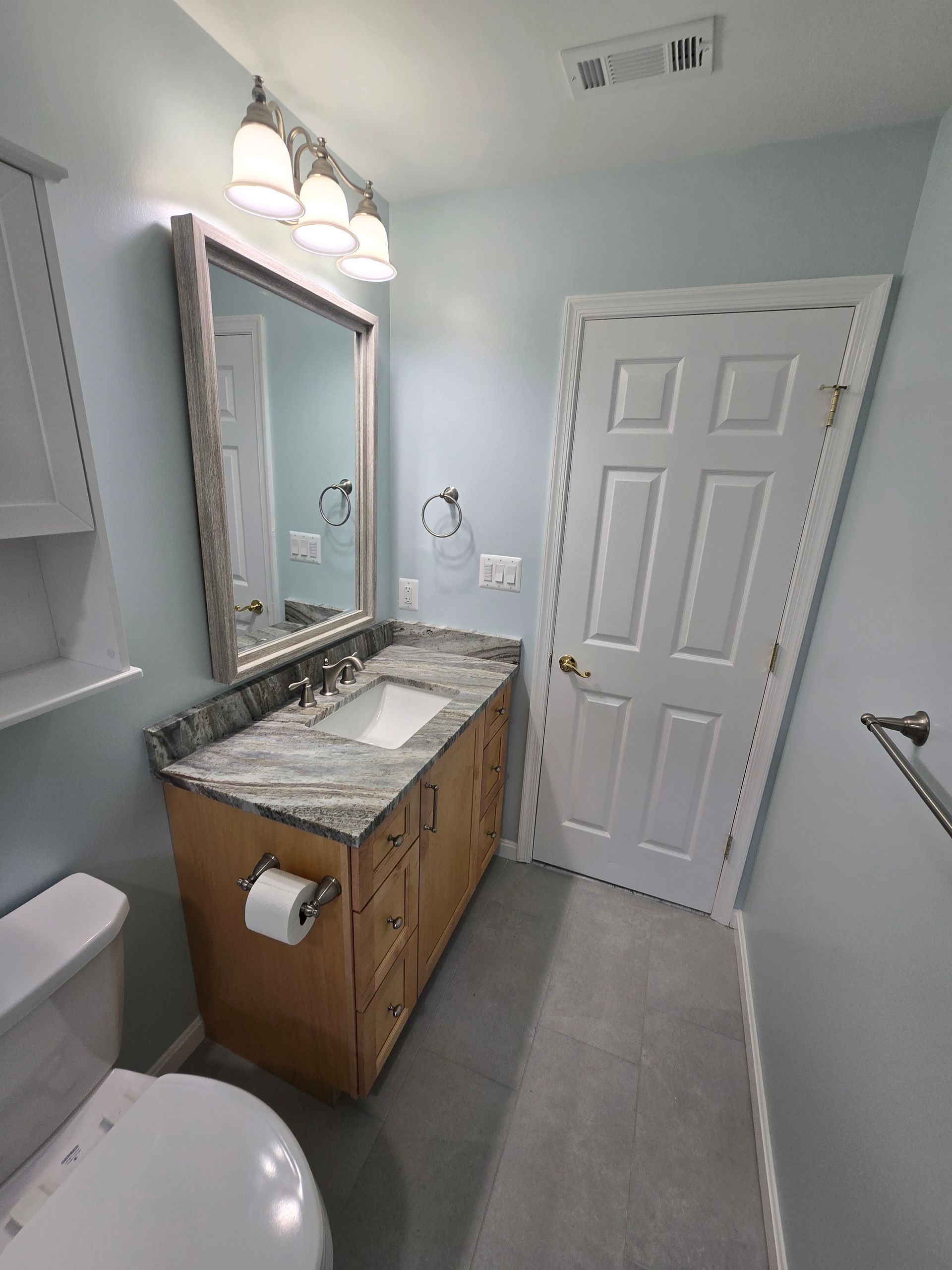 Bathroom with light blue walls, vanity, and toilet.