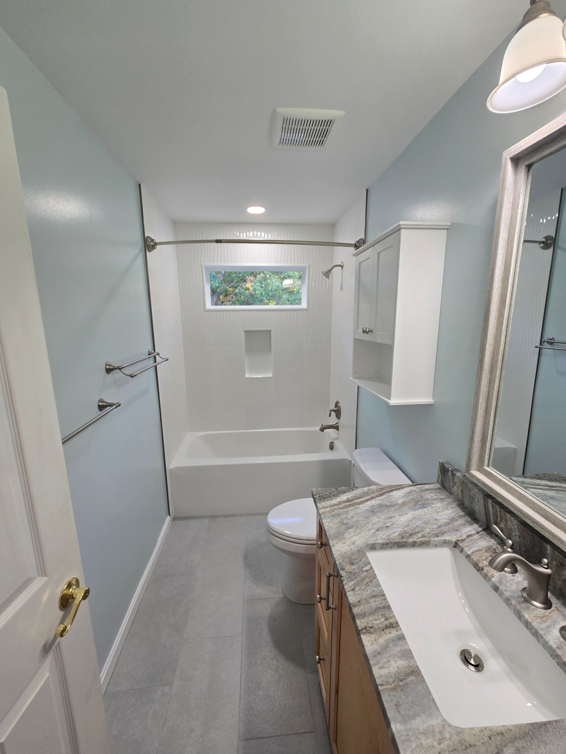 Bathroom with light blue walls, gray tile floor, white tub/shower, and vanity with granite countertop.