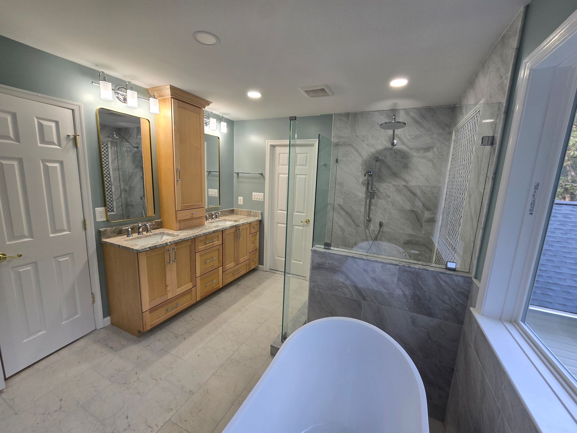 Bathroom with wooden cabinets, glass shower, freestanding tub, and a window.