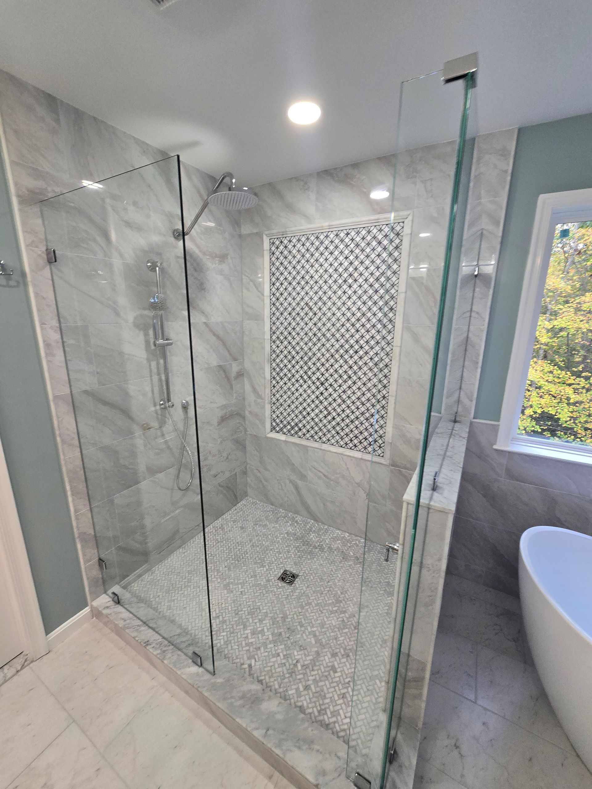 Modern bathroom with glass shower enclosure, gray marble tile, mosaic accent, and pebble shower floor.