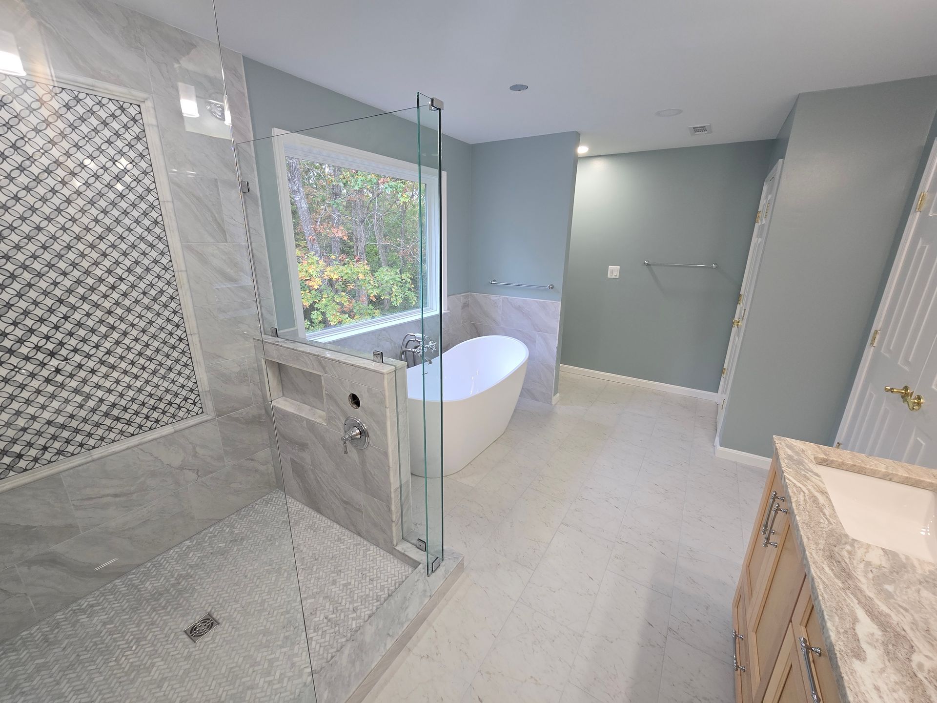 Modern bathroom with a white tub, walk-in shower, and light blue walls.