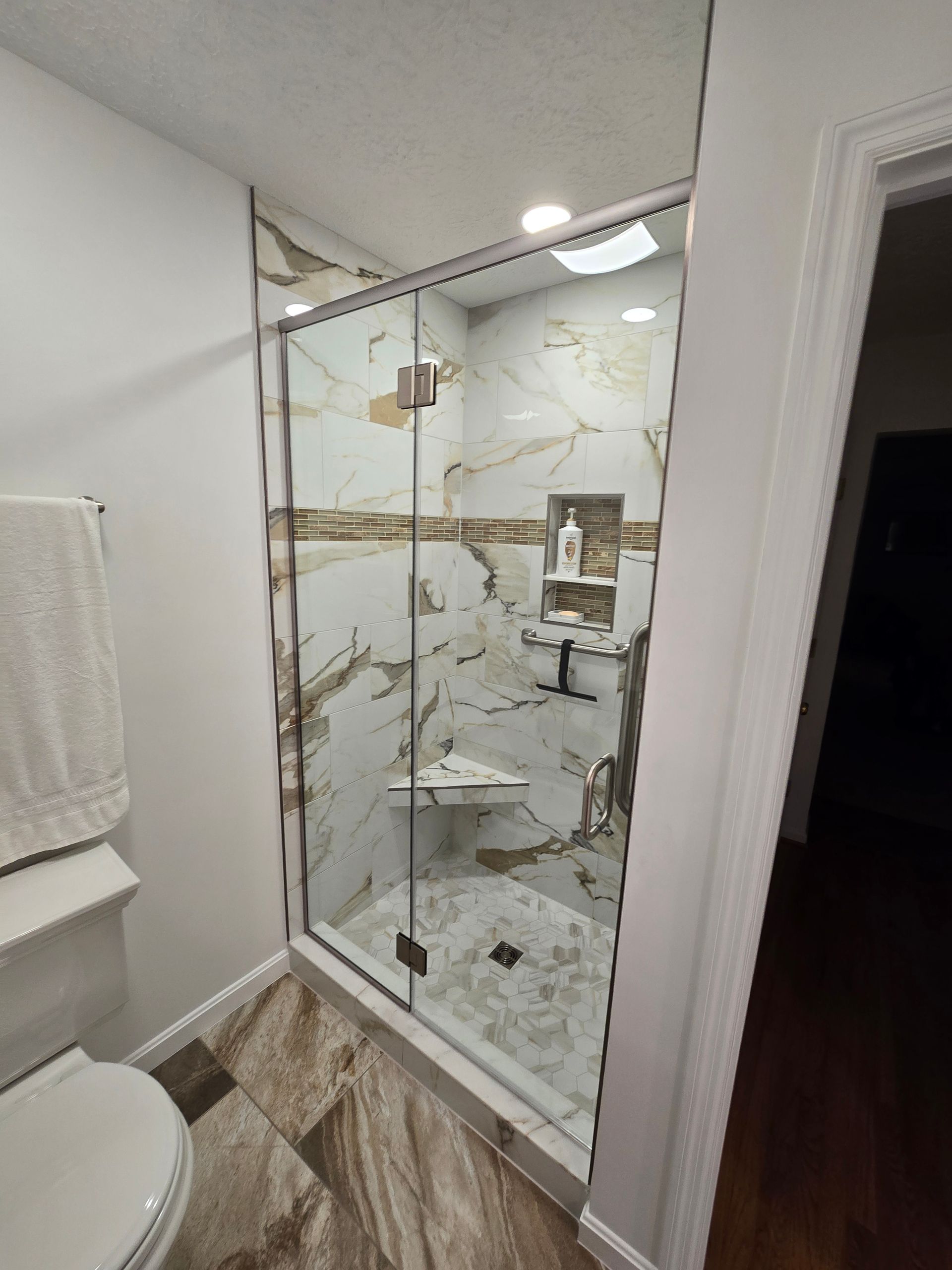 Glass-enclosed shower with marble-like tile, recessed shelf, and a built-in bench.