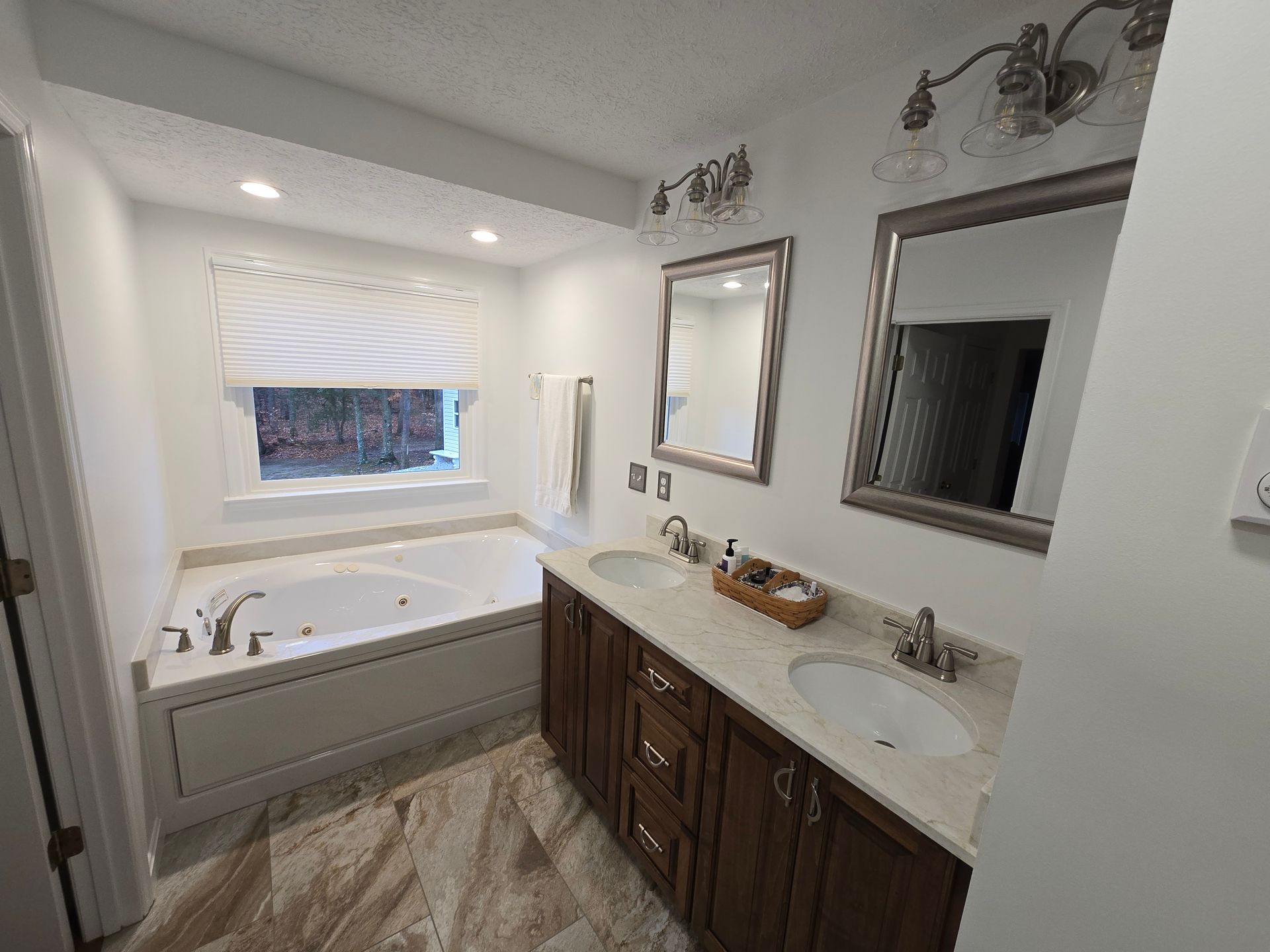 Bathroom with a tub and double sink vanity. Neutral colors, recessed lighting, and mirrors.