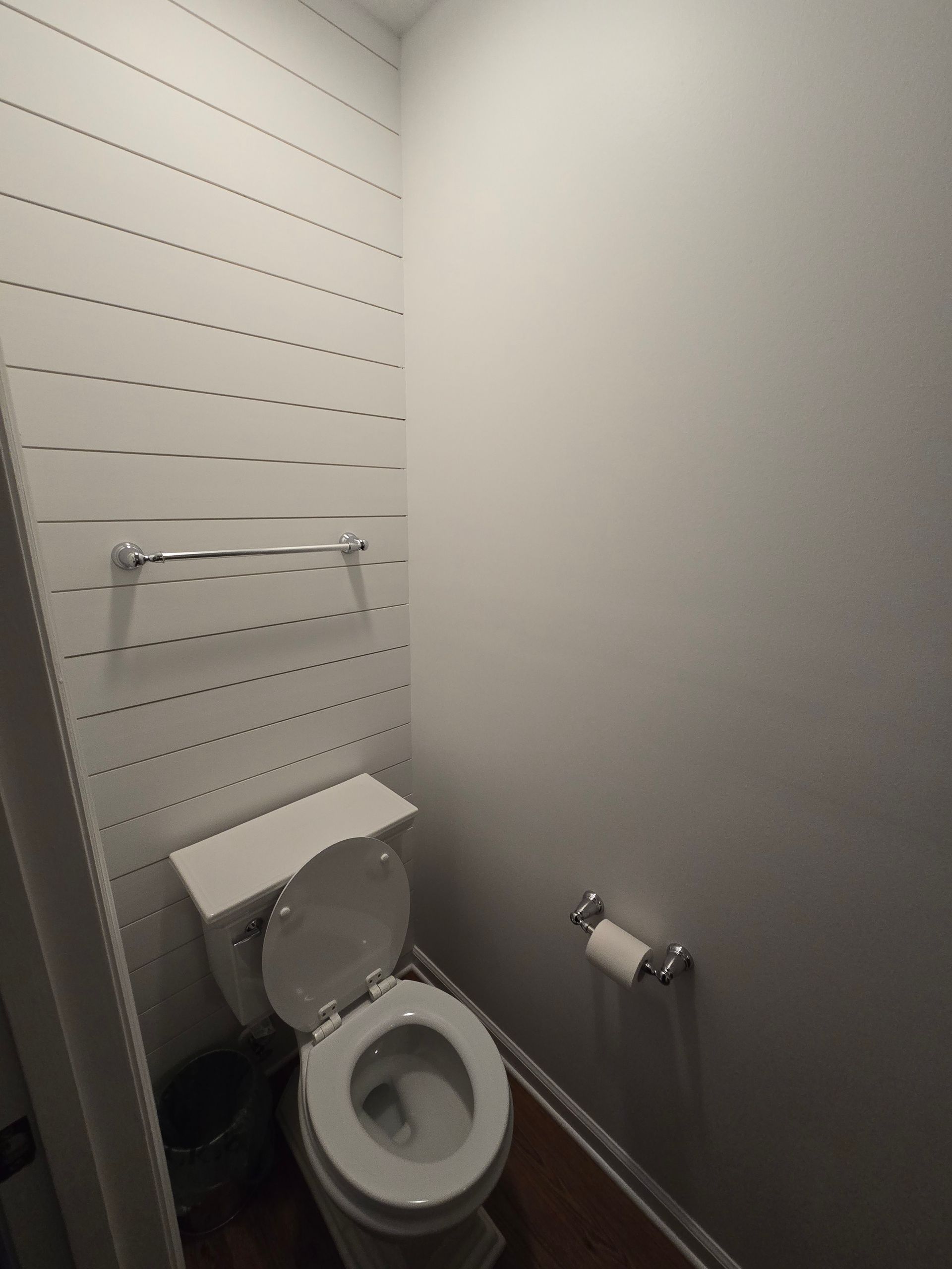 Small bathroom with toilet and paper holder; shiplap wall; gray wall; chrome fixtures.