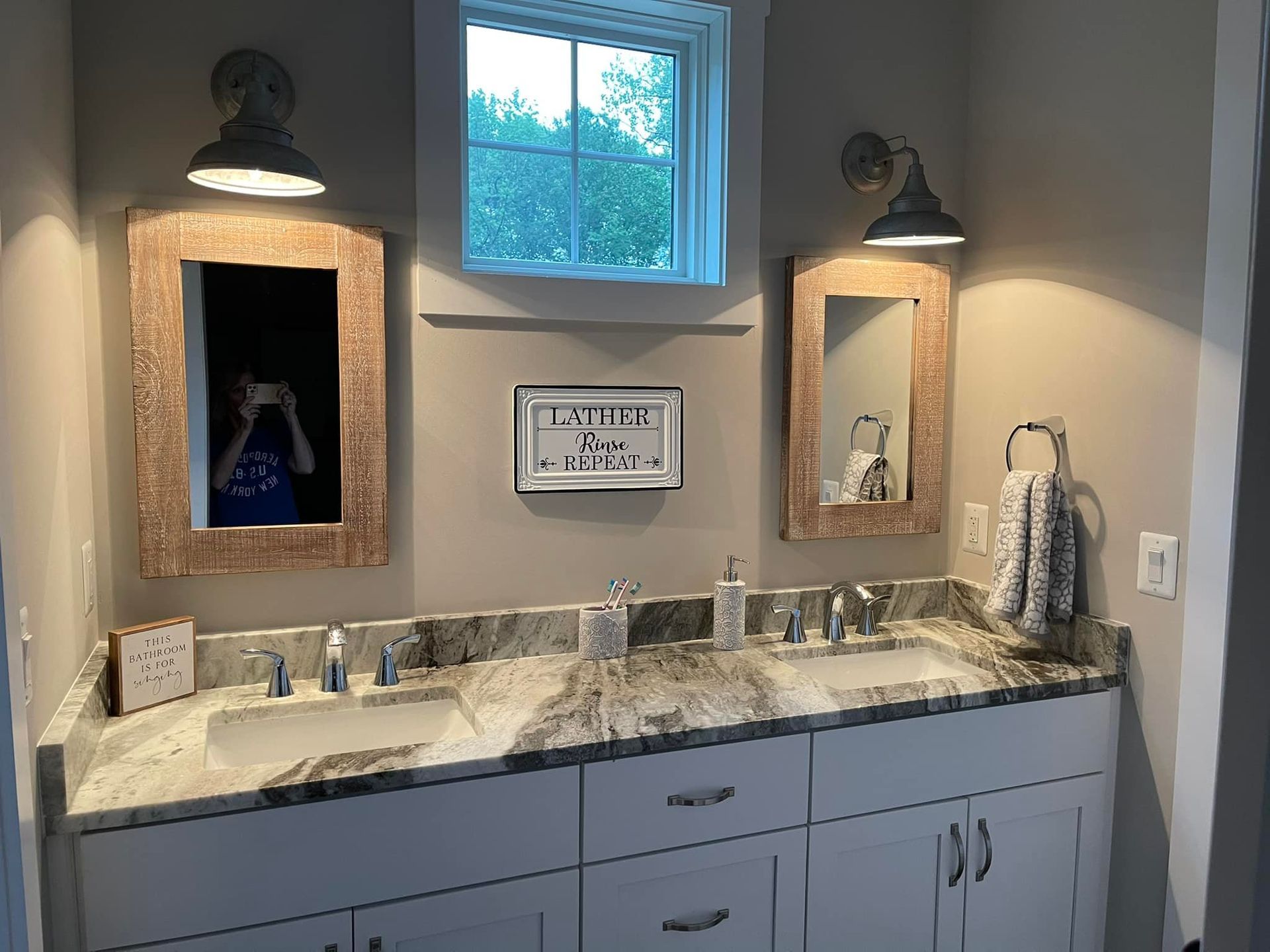 Bathroom with double sinks, two mirrors with sconce lights, and a small window.