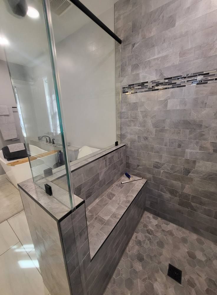 Modern bathroom shower with gray tile walls, glass enclosure, and built-in bench.