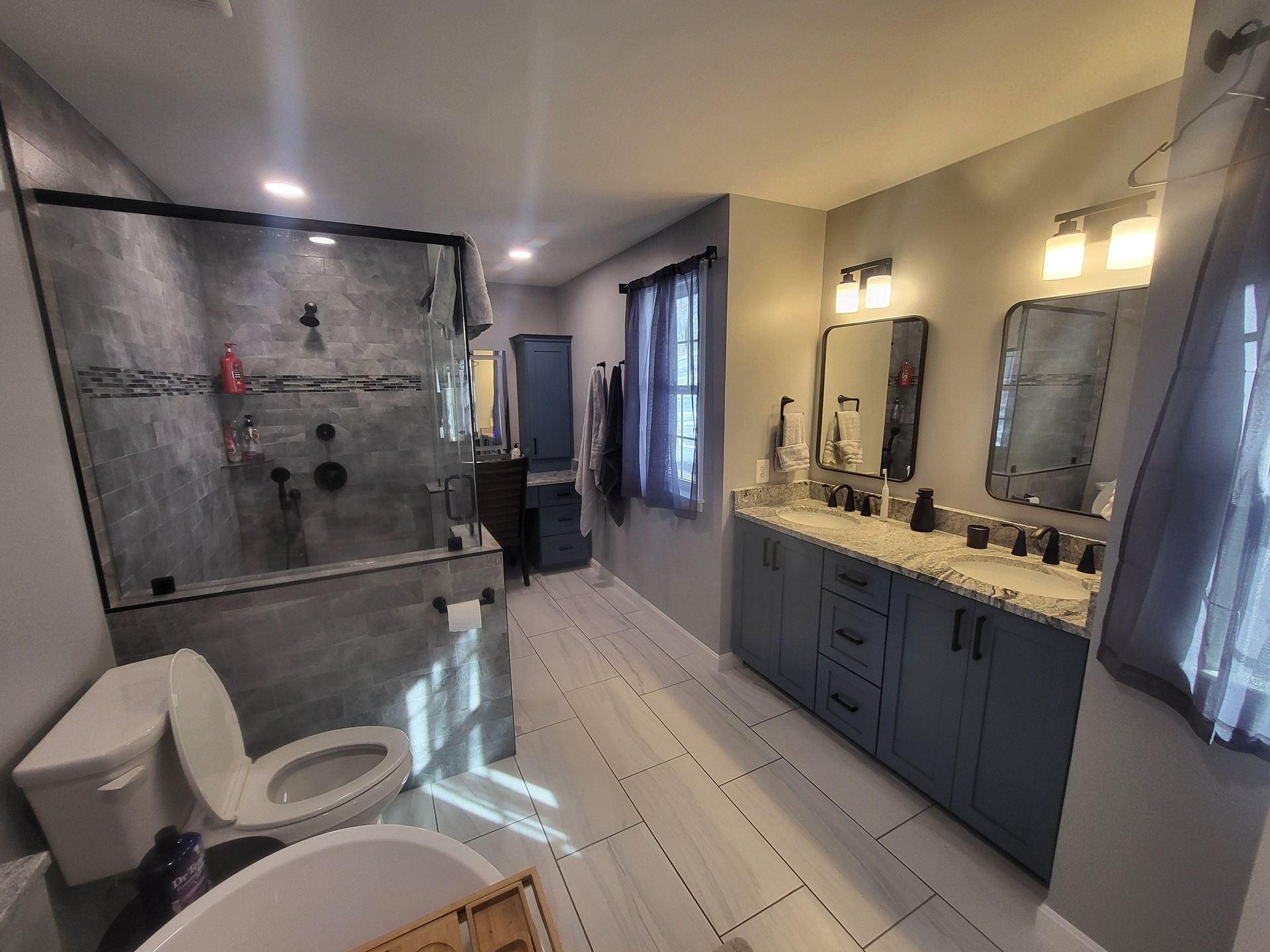 Bathroom with a glass shower, dual sinks, blue cabinets, and gray walls.