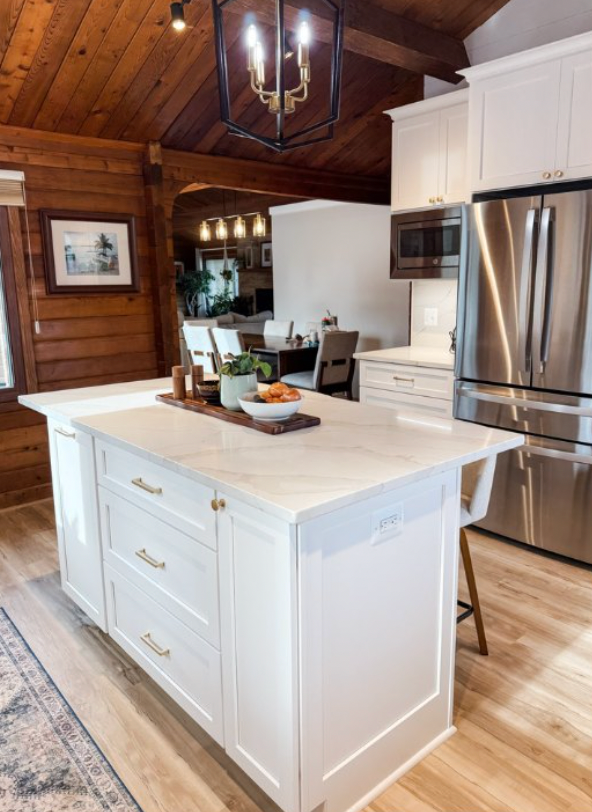 White kitchen with island, stainless steel refrigerator, wooden ceiling, and dining area in the background.