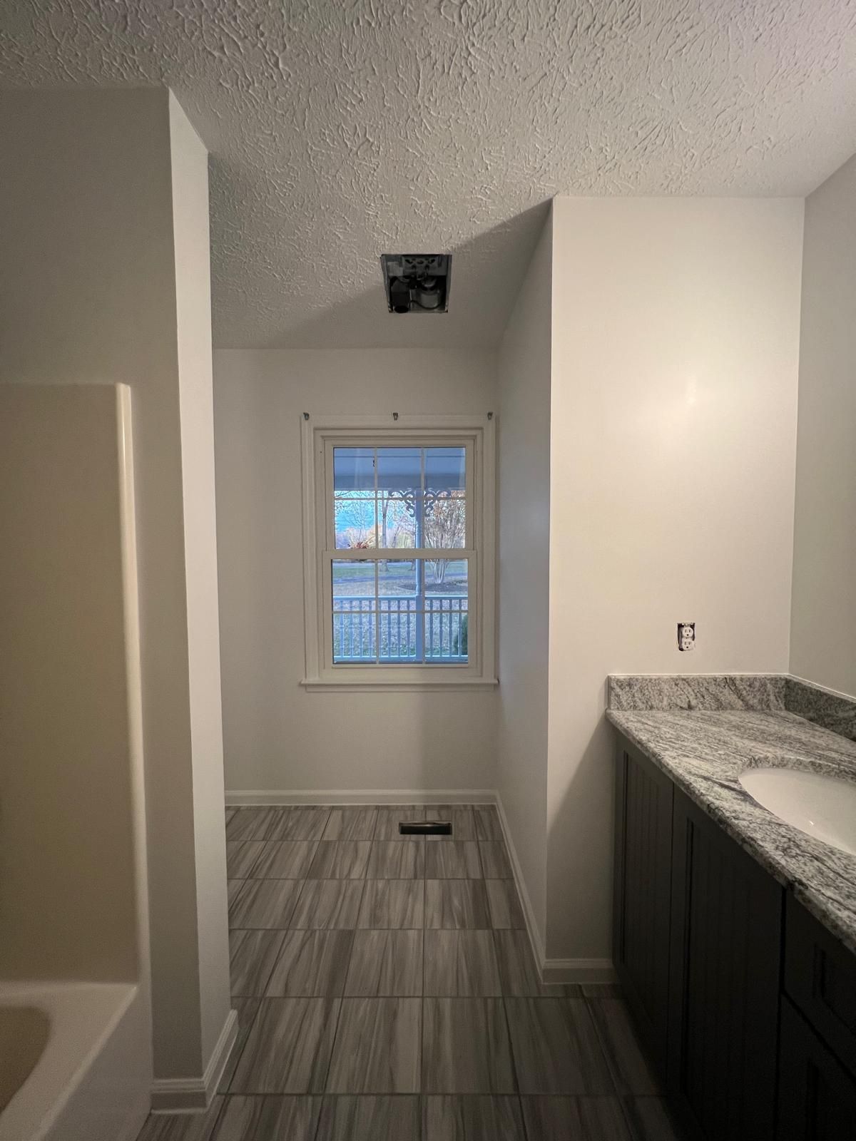 Bathroom interior with window, dark vanity, and gray tiled floor. White walls and ceiling.