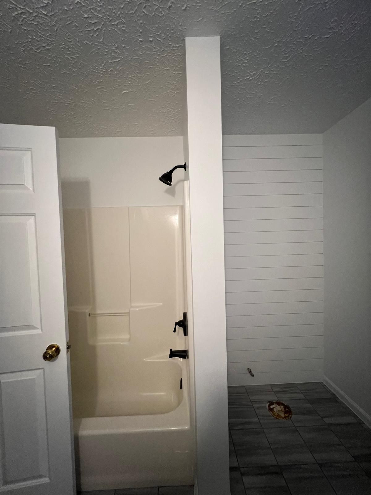Bathroom with a white shower, white door, and tiled floor. A white wall separates the shower.