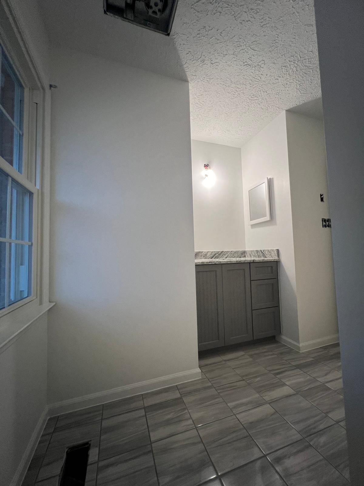 Bathroom interior with gray vanity, tile floor, white walls, and a window.