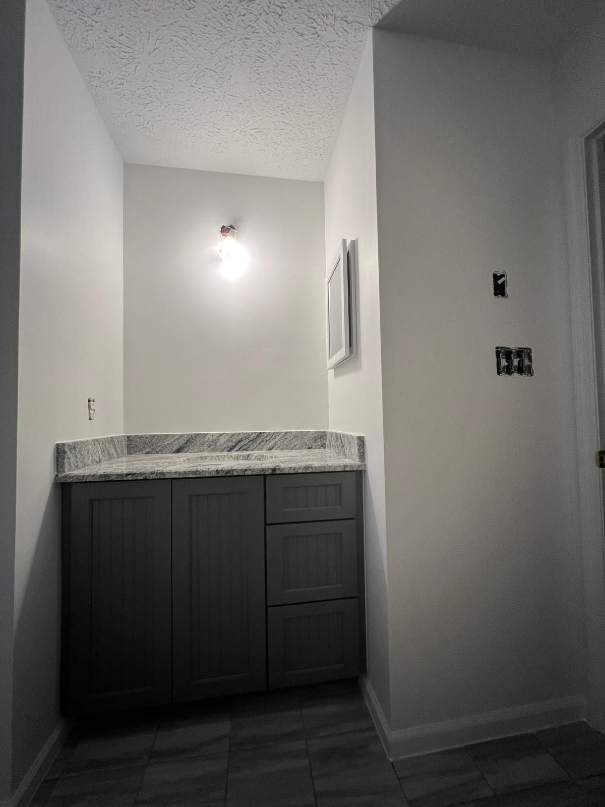 Gray vanity with granite countertop in a small bathroom with light gray walls; light fixture installed.