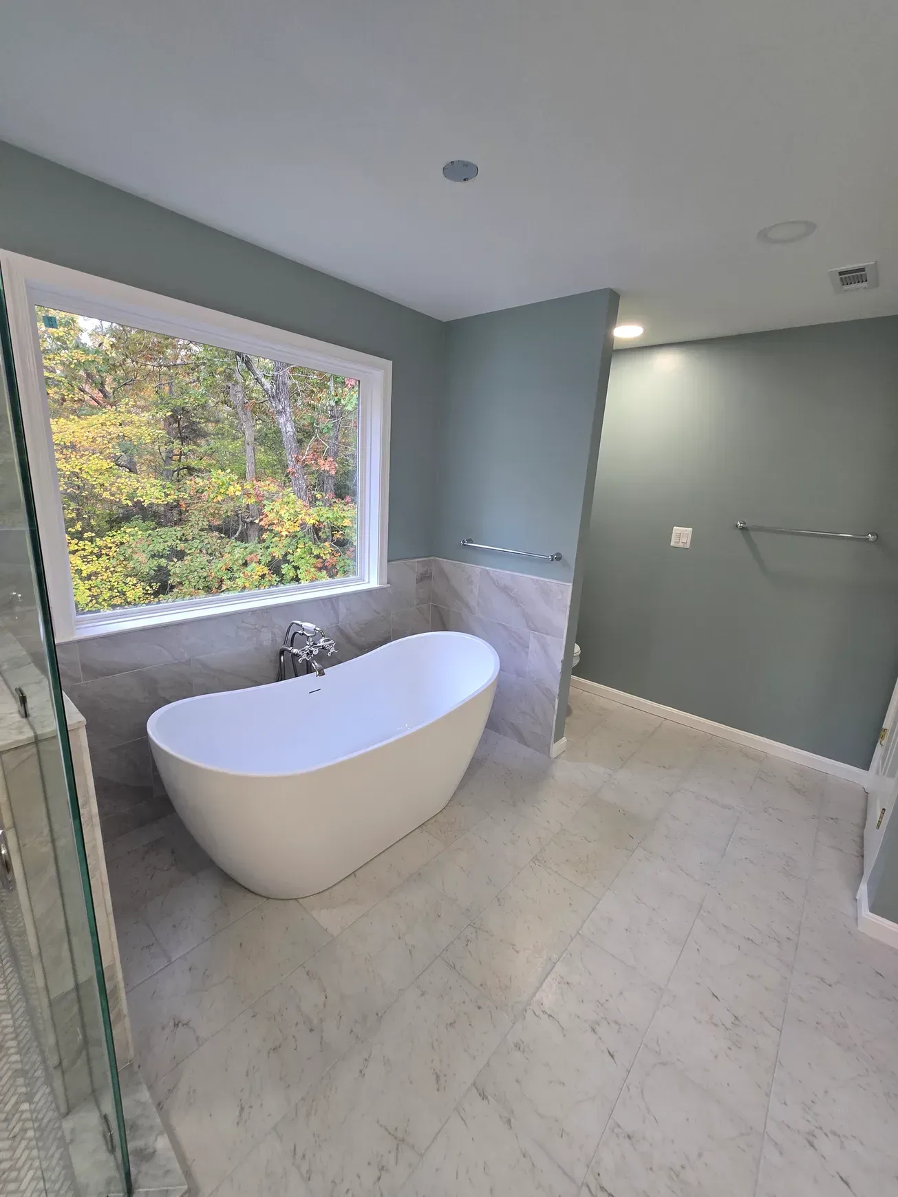 Modern bathroom with a white freestanding tub, large window, and light gray tile floor.