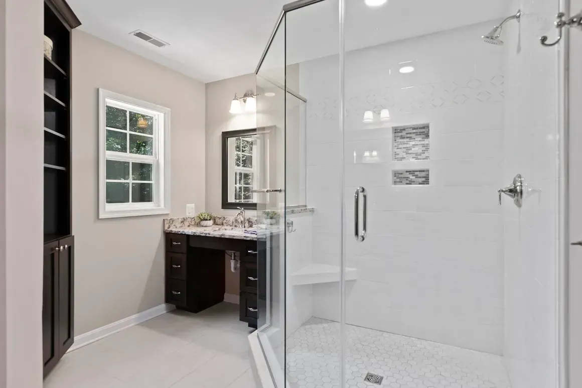 Modern bathroom with a glass shower, vanity, and built-in shelving. White and dark brown tones.