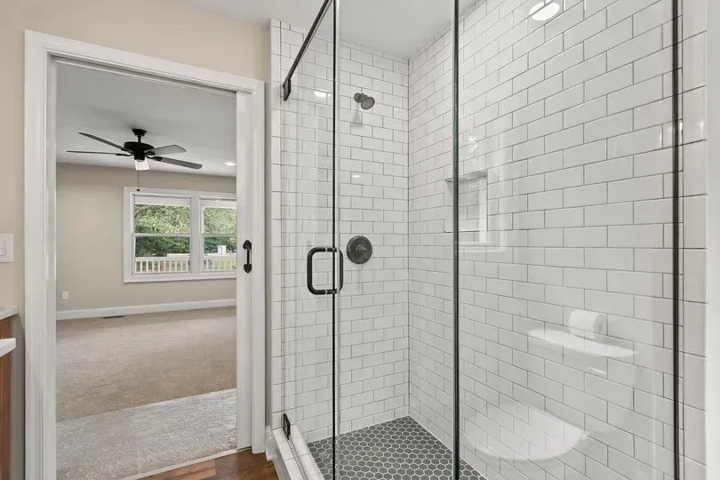Modern bathroom with glass shower, subway tile, and open doorway to bedroom.