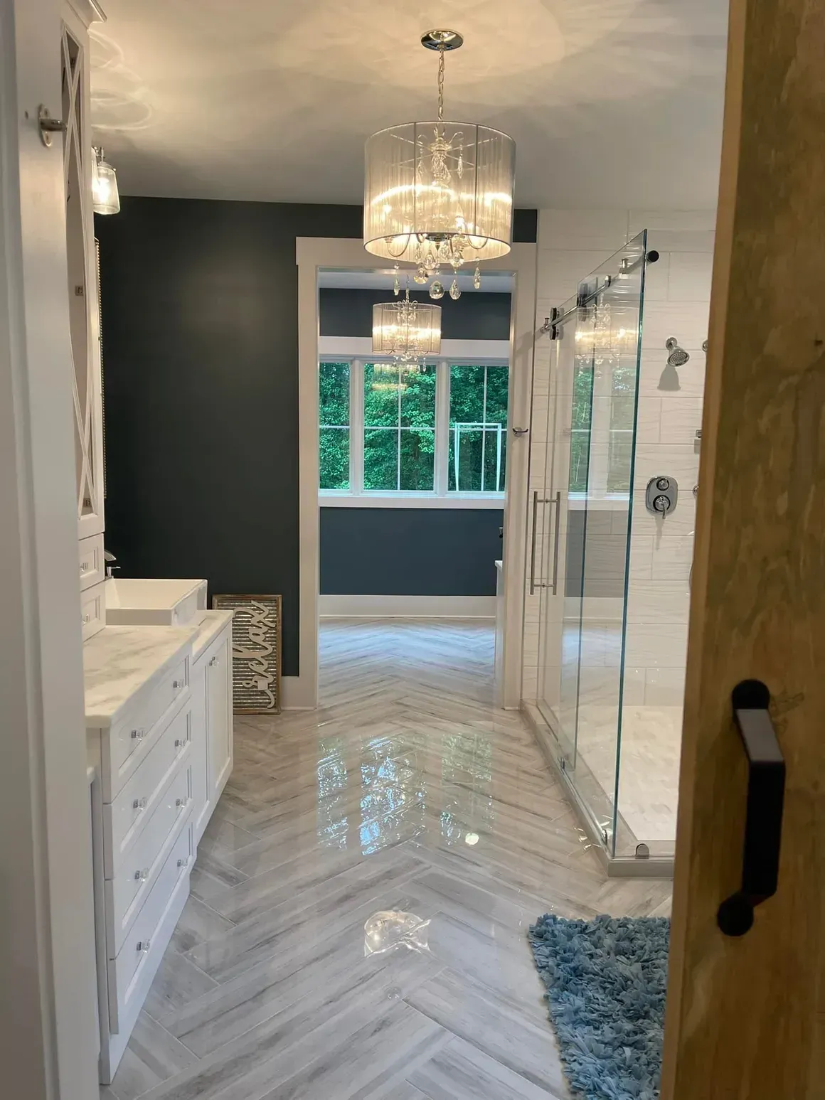 Bathroom with marble herringbone floor, white vanity, glass shower, and crystal chandeliers.