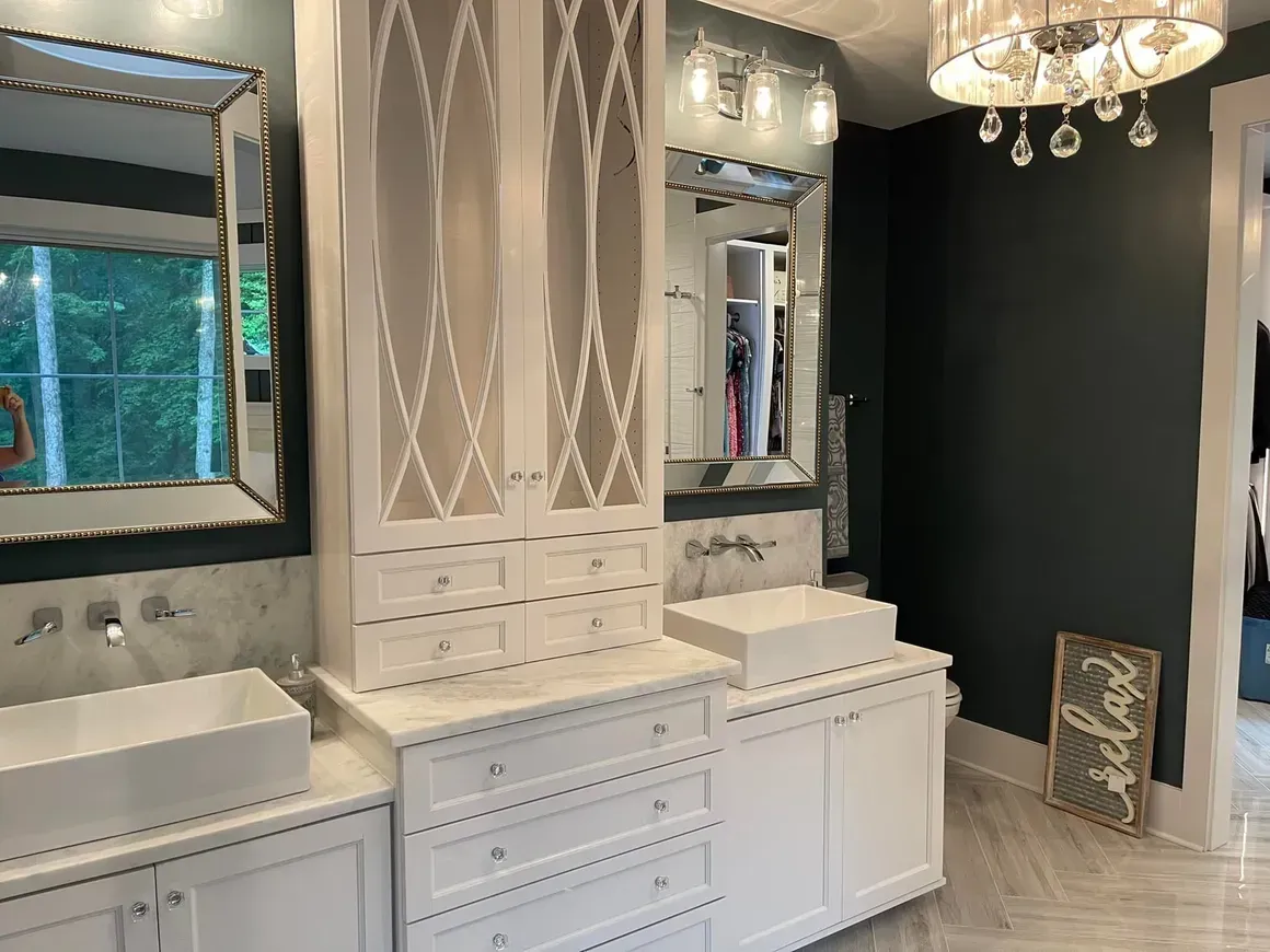 White bathroom with vanity, mirrors, cabinets, and a chandelier. Dark gray walls, and a marble floor.