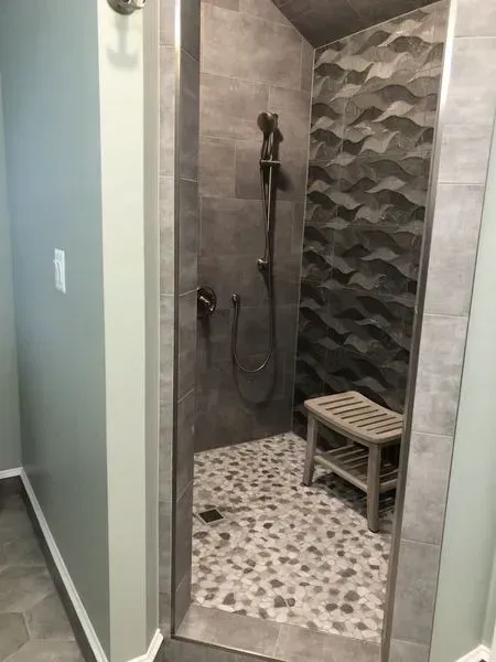 Gray tile shower with stone floor and wooden bench.