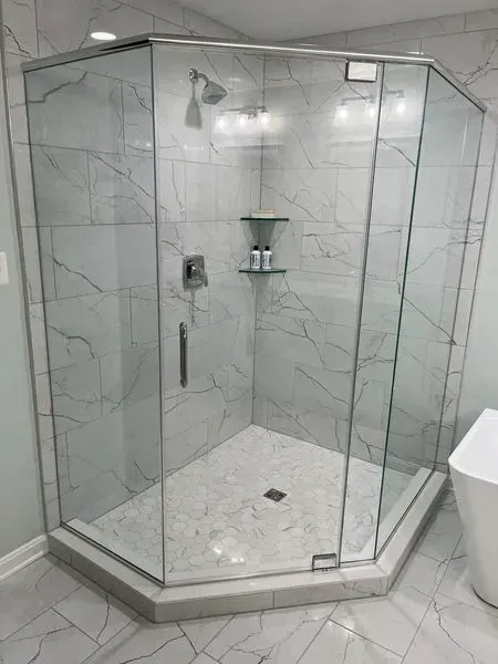 Glass-enclosed shower with white marble tile, chrome fixtures, and a glass shelf in a modern bathroom.