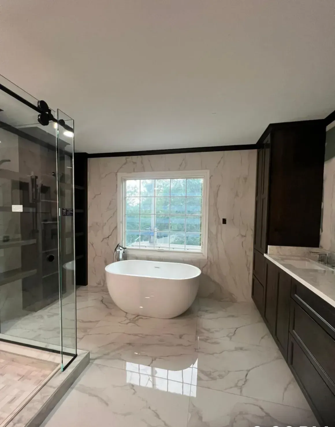 Bathroom with a freestanding tub, glass shower, dark cabinetry, and marble-look tile.
