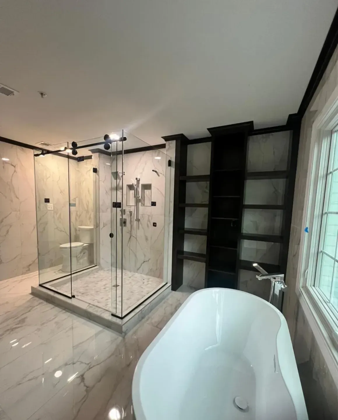 Luxurious modern bathroom with a glass shower, white tub, and built-in shelves.