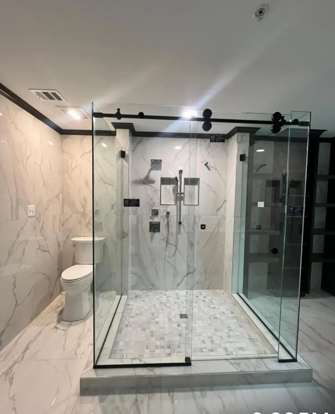 Spacious bathroom with glass shower enclosure, marble tile, and a black sliding shower door.