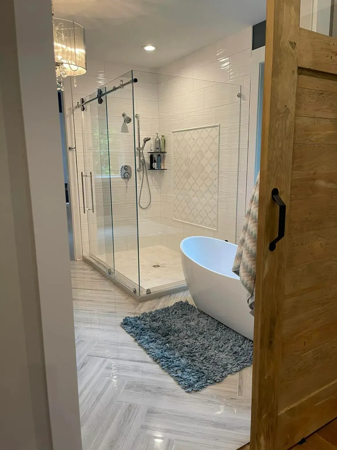Luxurious bathroom with a glass shower, white soaking tub, and wooden door.