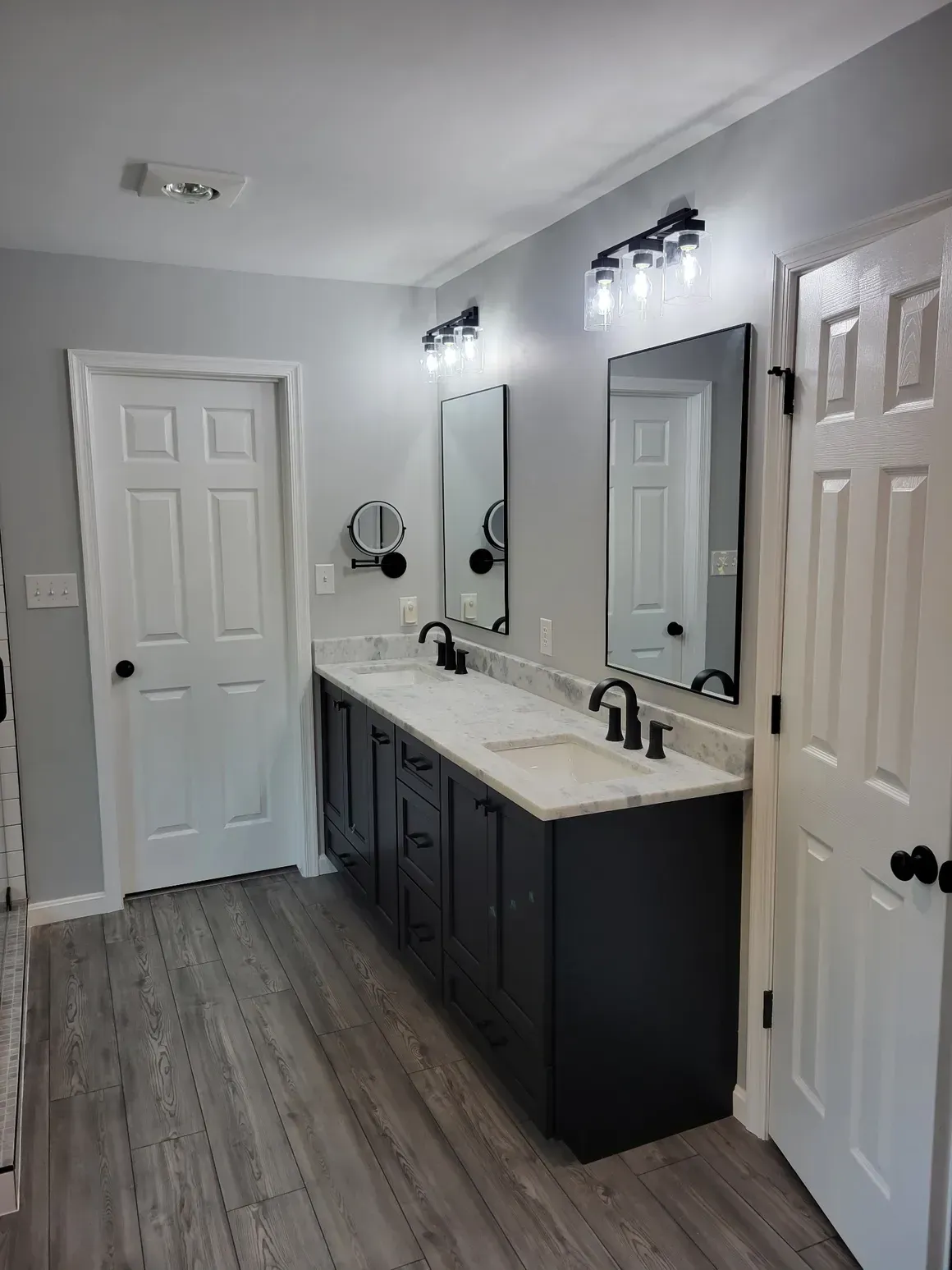 Bathroom with dark vanity, white countertops, two mirrors, and gray walls.