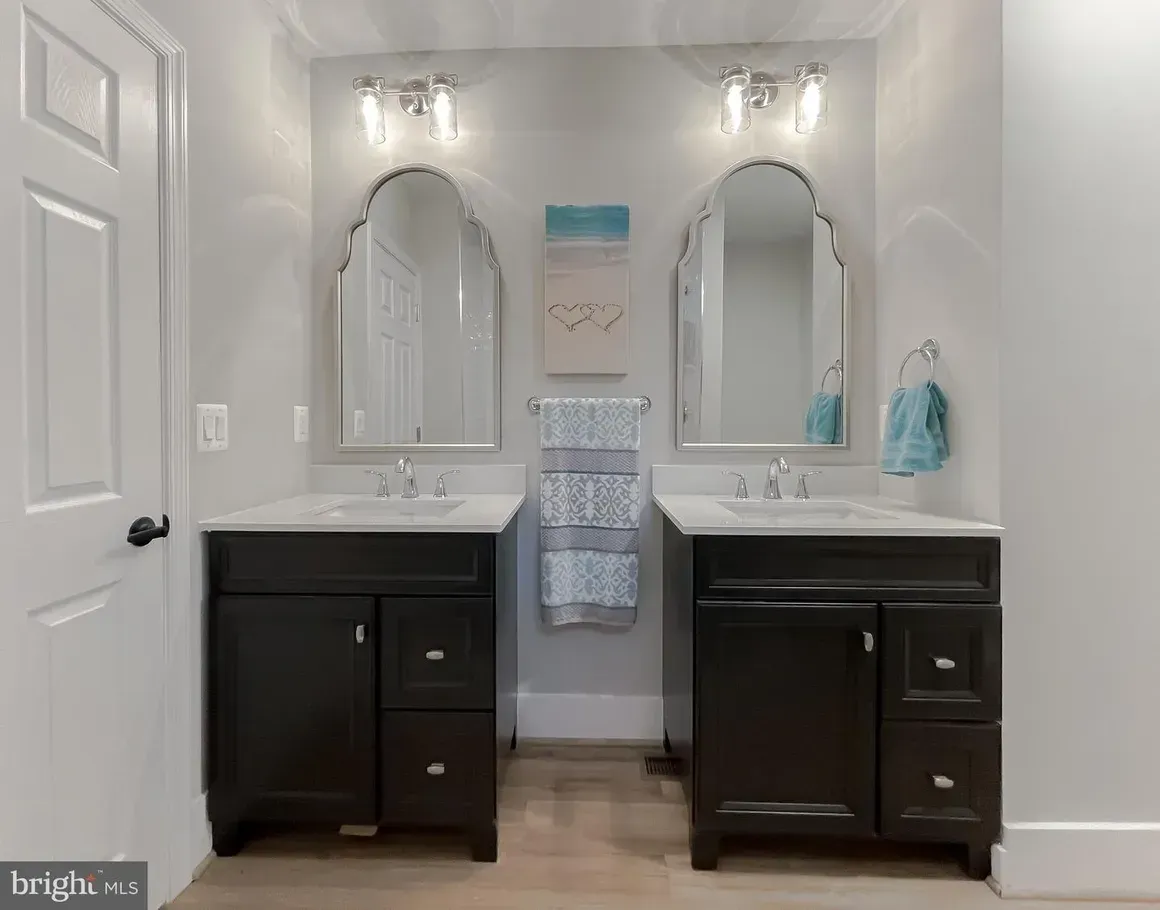Bathroom with two dark vanities, arched mirrors, and light fixtures. White walls and door.