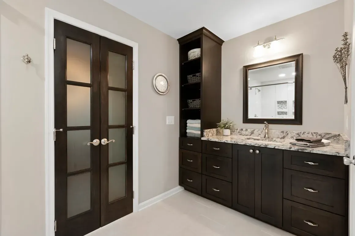 Bathroom with dark wood vanity, built-in shelves, and frosted-glass doors.