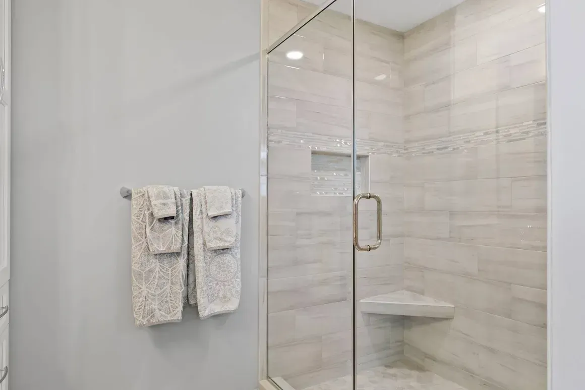 Bathroom with glass shower, light gray walls, and white tiled interior. Two towels hang on a bar.