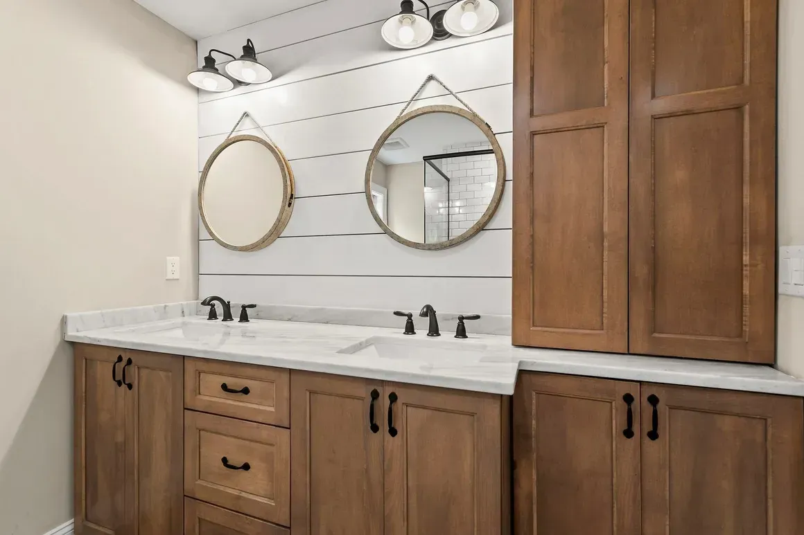 Bathroom vanity with two round mirrors, brown cabinets, white countertop, and shiplap wall.