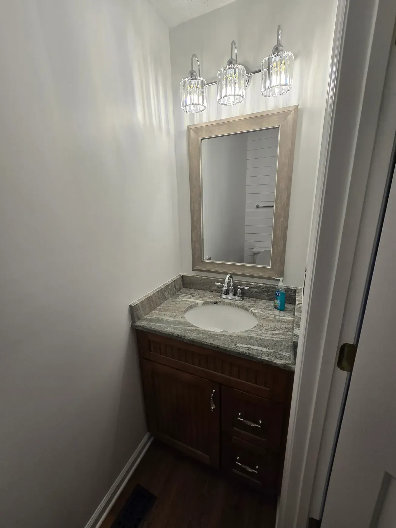Small bathroom with brown vanity, granite countertop, mirror, and a light fixture.