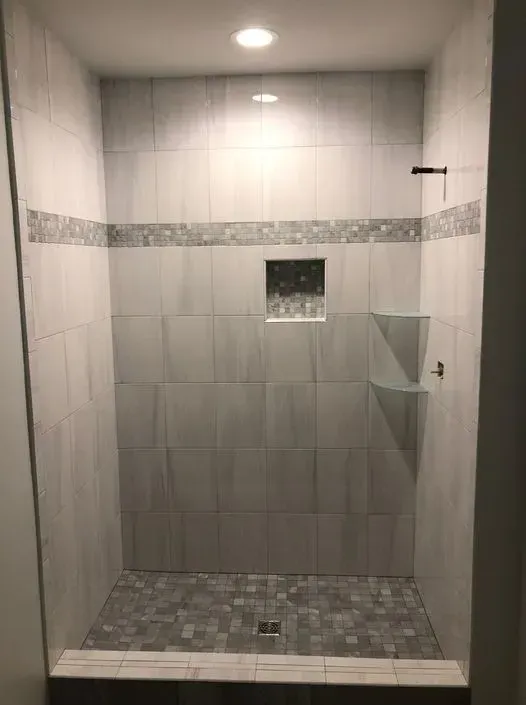 A tiled shower stall with grey tiles, decorative border, and built-in shelving and niche.
