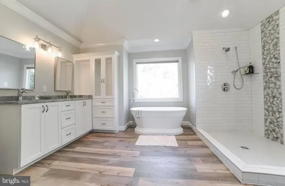 Spacious white bathroom with a freestanding tub, large shower, double vanity, and wood-look flooring.