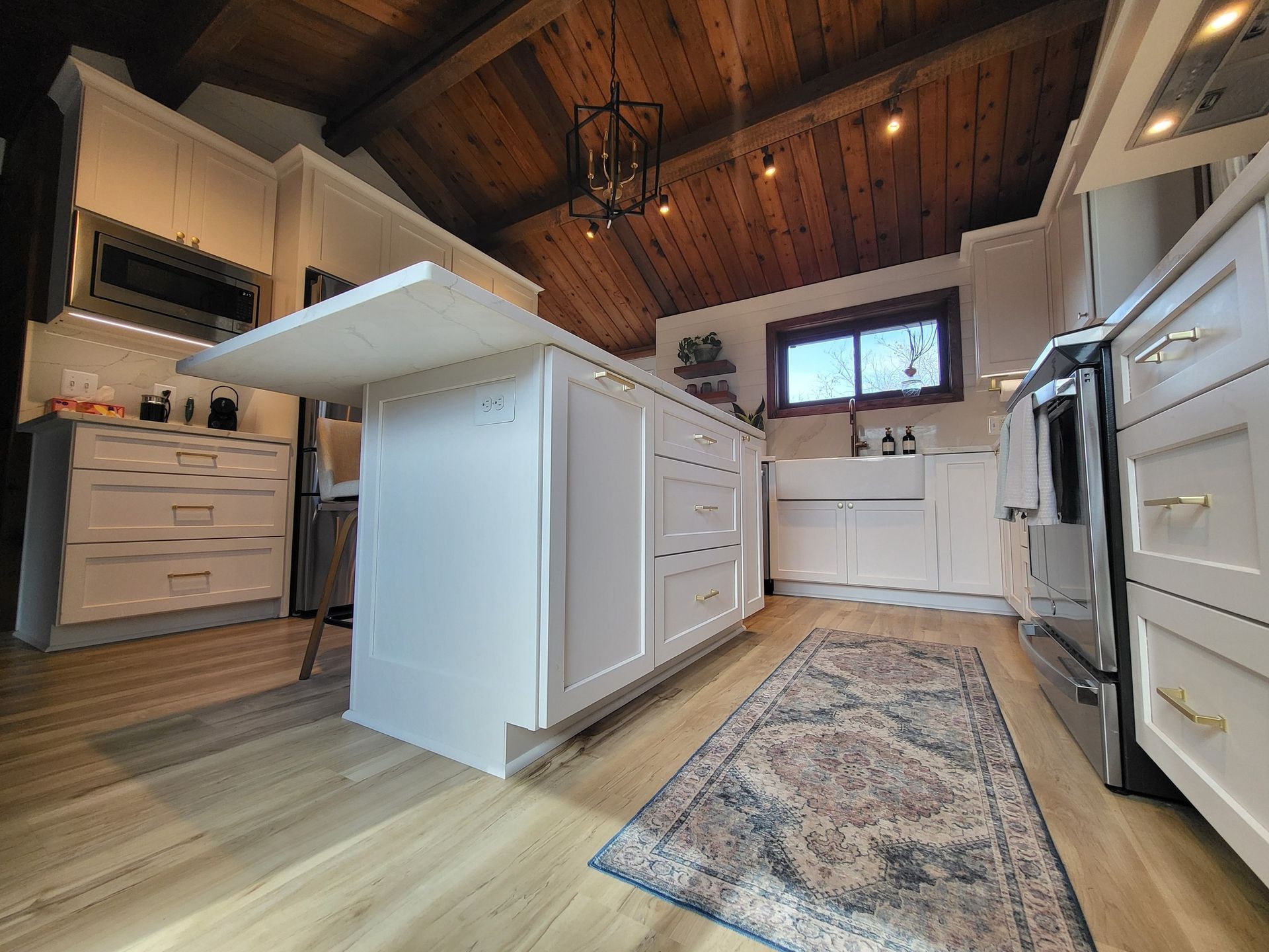 White kitchen with island, wooden ceiling, and patterned rug.