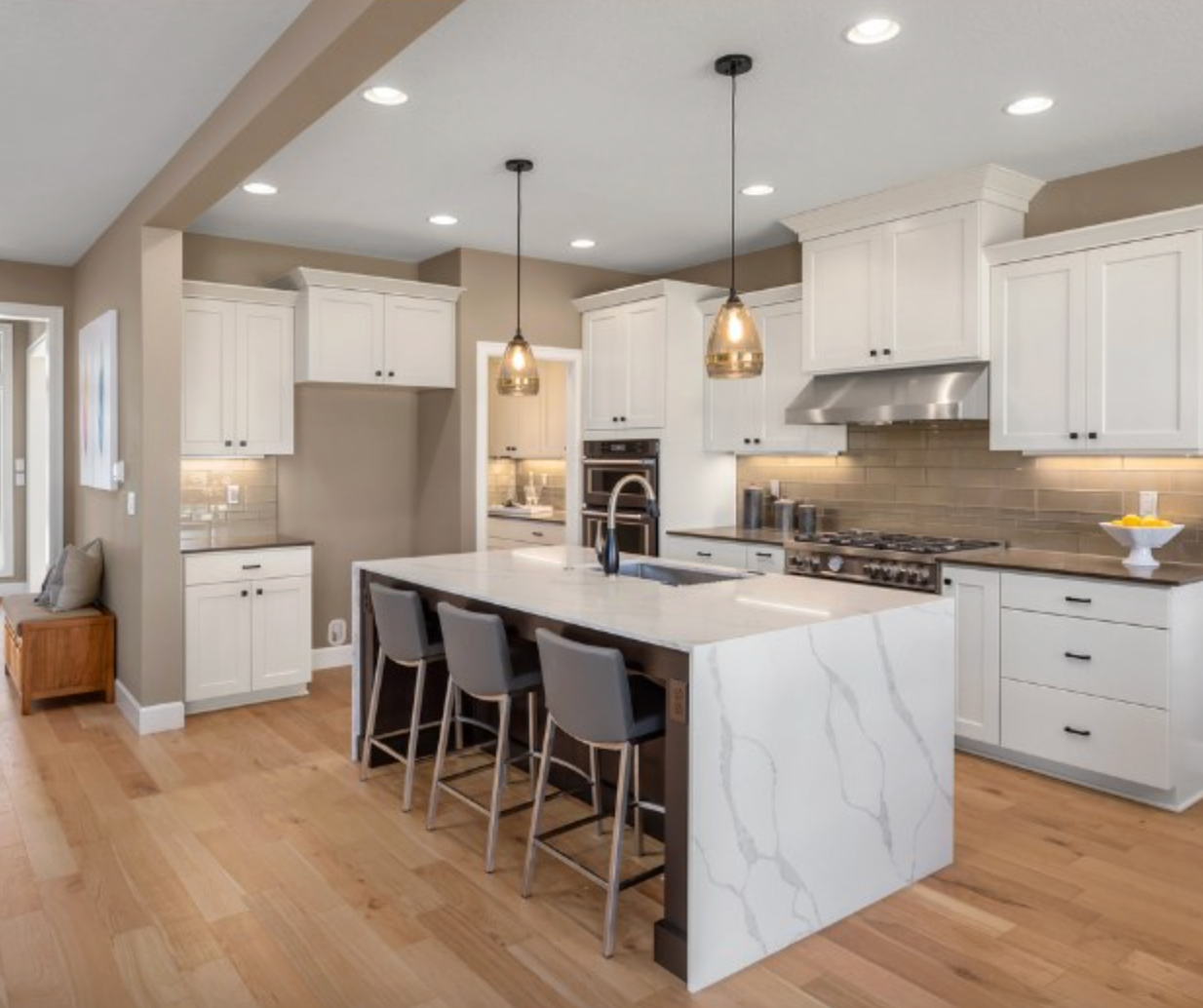 Modern kitchen with white cabinets, marble island, wood floor, and pendant lights.